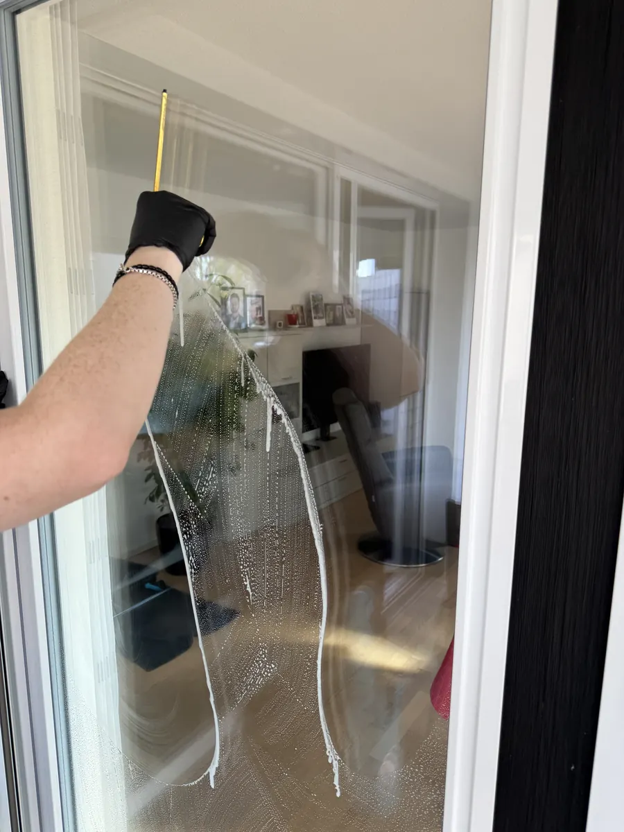 Fensterreinigung im Privathaushalt: Glasscheibe einer Balkontür wird mit dem Abzieher streifenfrei gereinigt