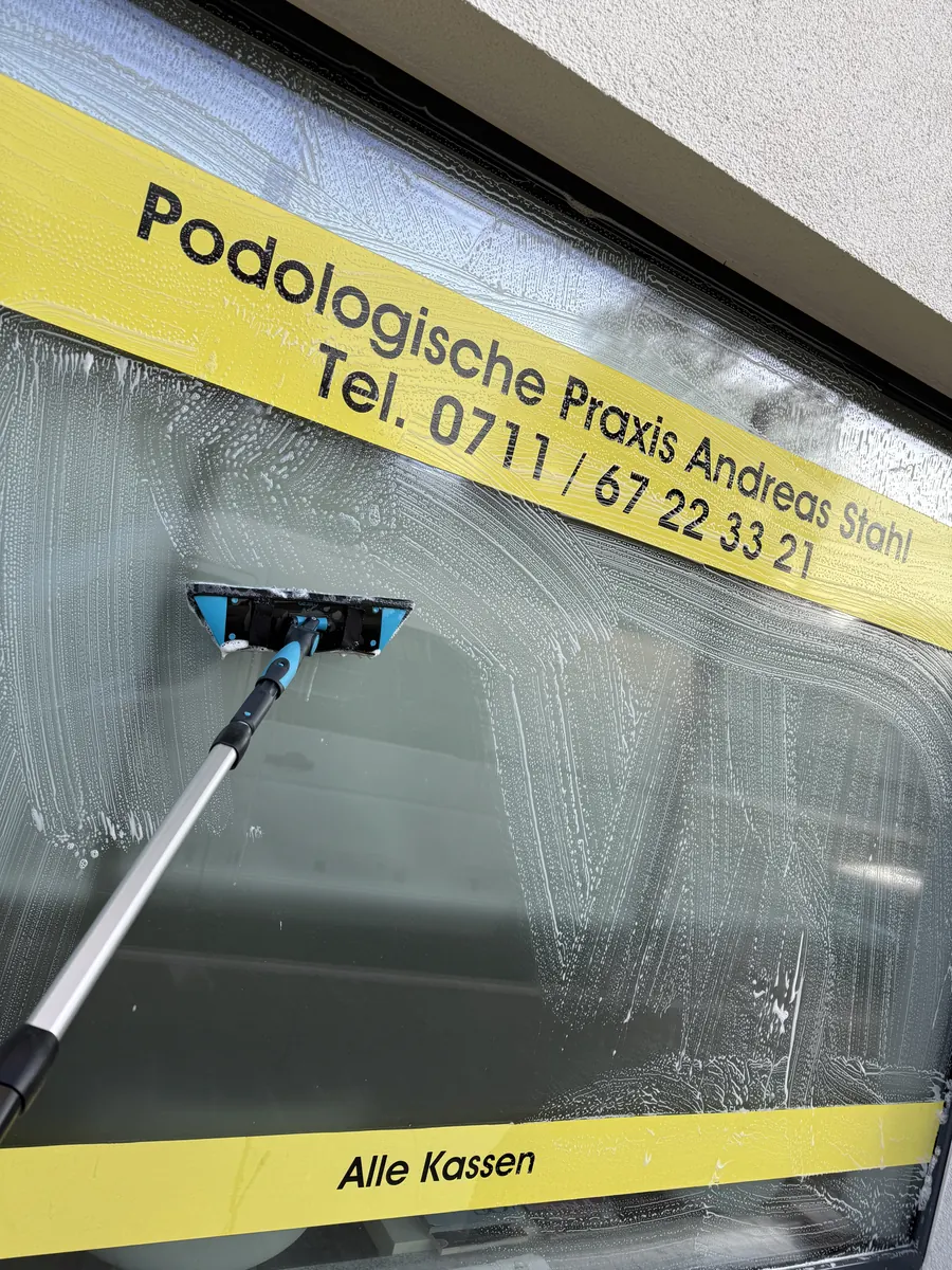 Schaufensterreinigung: beschriftete Schaufensterscheibe einer Praxis wird mit Einwascher und Teleskopstange gereinigt